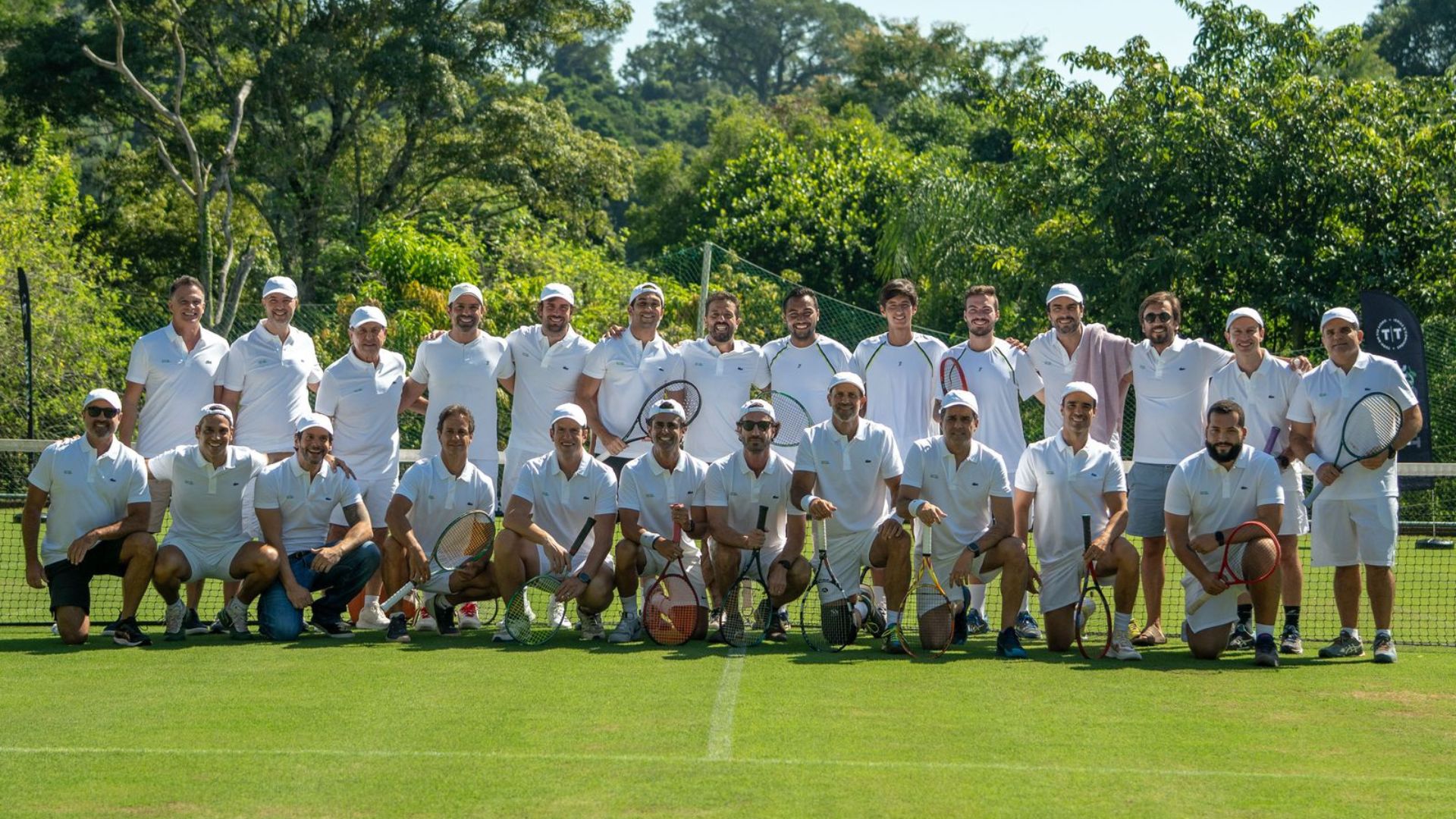 Empresários jogando tênis em quadra de grama durante o evento 'Na Grama com a TT'